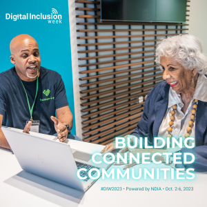 An older woman smiles while learning how to use a laptop with an instructor or guide, she is radiating empowerment and enthusiasm. Accompanied by “Building Connected Communities” and the Digital Inclusion Week Logo.