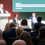 Business conference featuring panel discussion with professionals and audience interaction at modern event venue under dim lighting. By Anton Gvozdiko